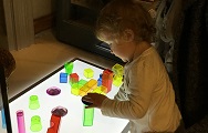 A young child plays with light-up coloured blocks during a mini museum play session